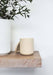 Cream Himalayan candle by aery displayed next to cream plant pot sat on wooden shelf 