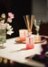 Red Positive Energy diffuser by Aery displayed next to vase on white flowers placed on white kitchen worktop 