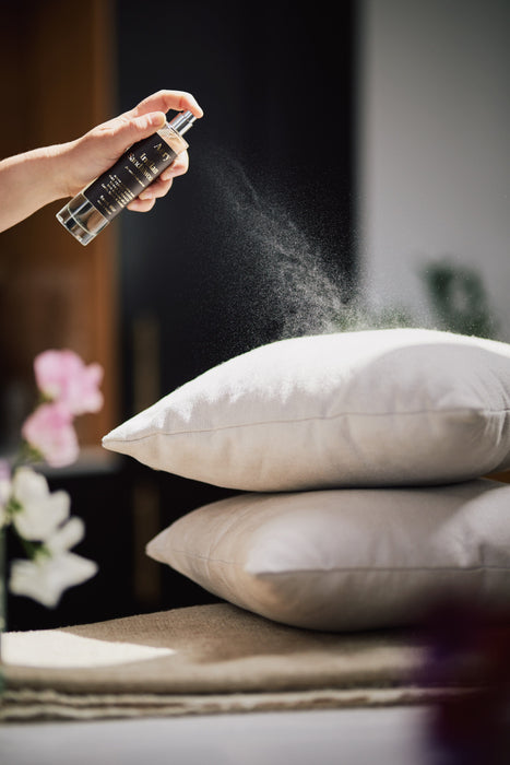 Black Indian sandalwood room mist by Aery displayed in hand spraying grey pillows 