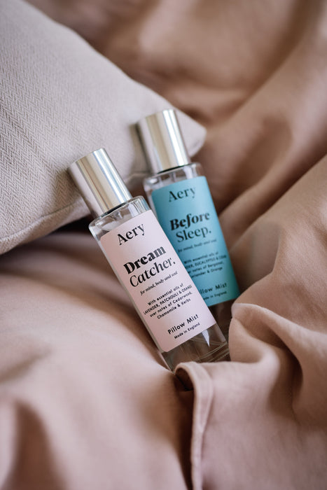 Blue Before Sleep pillow mist displayed next to Lilac Dream Catcher pillow mist placed on bed linen 