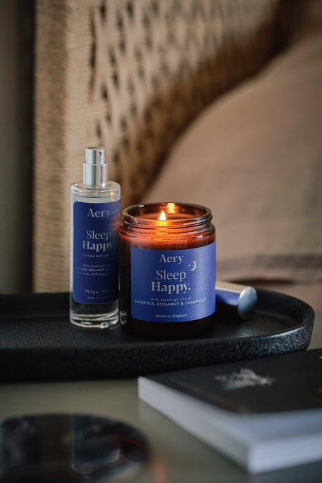 Blue Sleep Happy jar candle by aery displayed next to sleep happy pillow mist by aery placed on black tray on bedside table