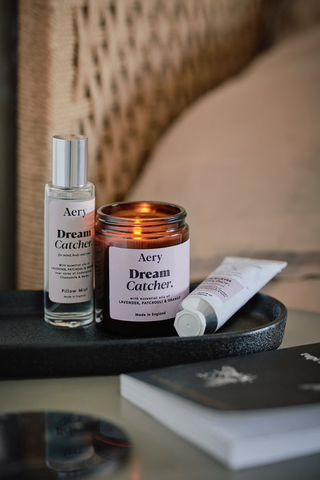 Lilac dream catcher jar candle by aery displayed next to dream catcher hand cream and pillow mist sat on black tray on bedside table