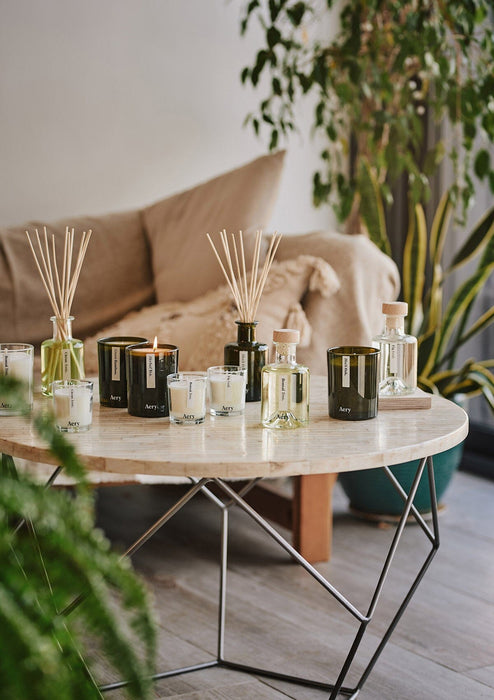 collection of botanical diffusers and candles by aery arranged on cream circle table in kitchen 