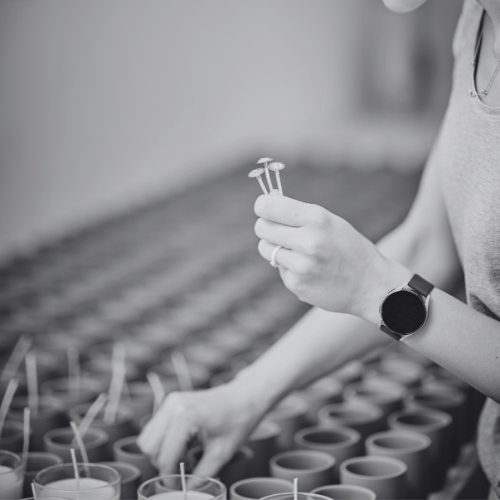 person sticking wicks to base of candle jars