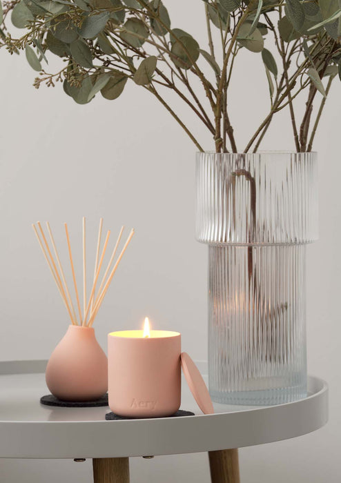 Pink Aztec Tuberose candle by aery displayed next to aztec tuberose diffuser and glass vase sat on grey circle table