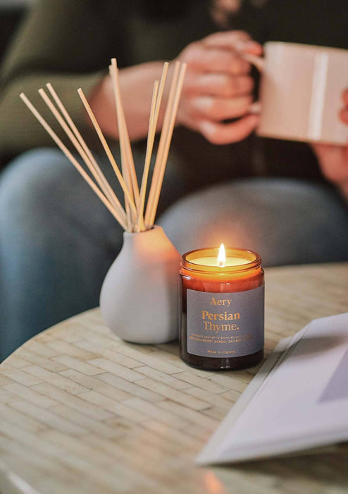 Grey Persian thyme jar candle by aery displayed next to Persian thyme diffuser by aery placed on cream table 